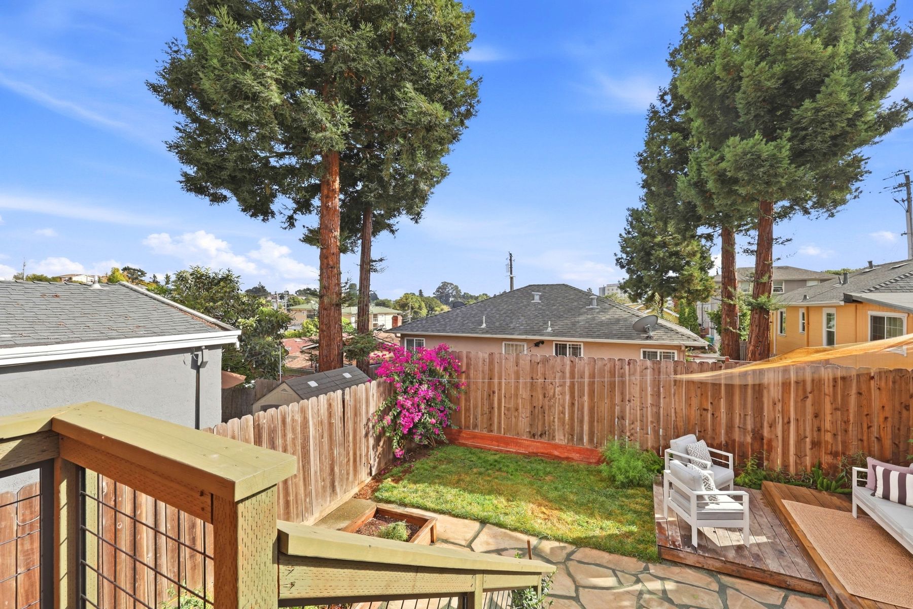 Backyard deck and lawn with mature trees beyond the fence